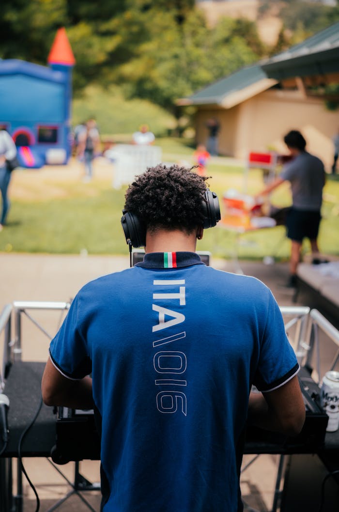 Offerings Back view of a DJ in a blue shirt performing at an outdoor event with headphones on.