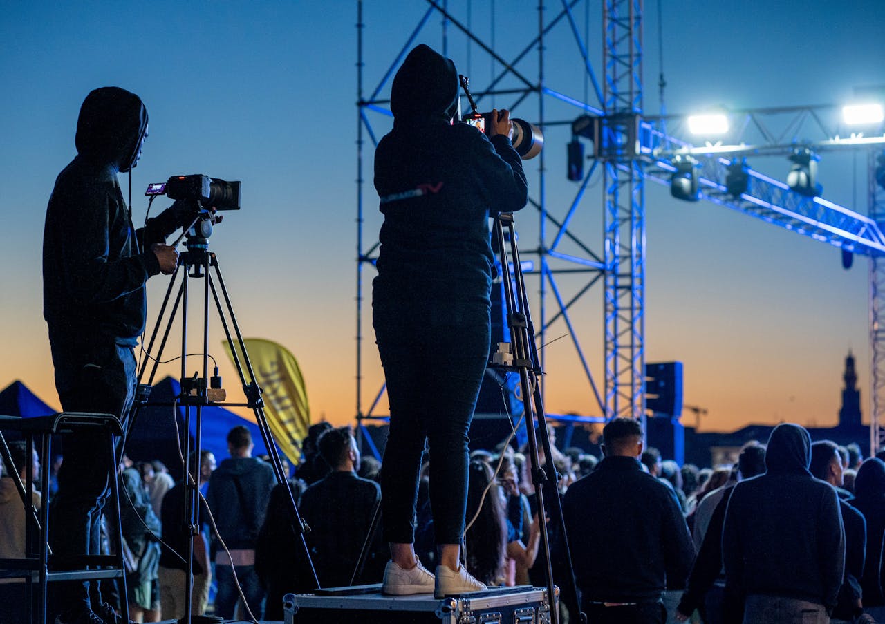 Photographers filming a vibrant outdoor event during a stunning sunset with an enthusiastic crowd.