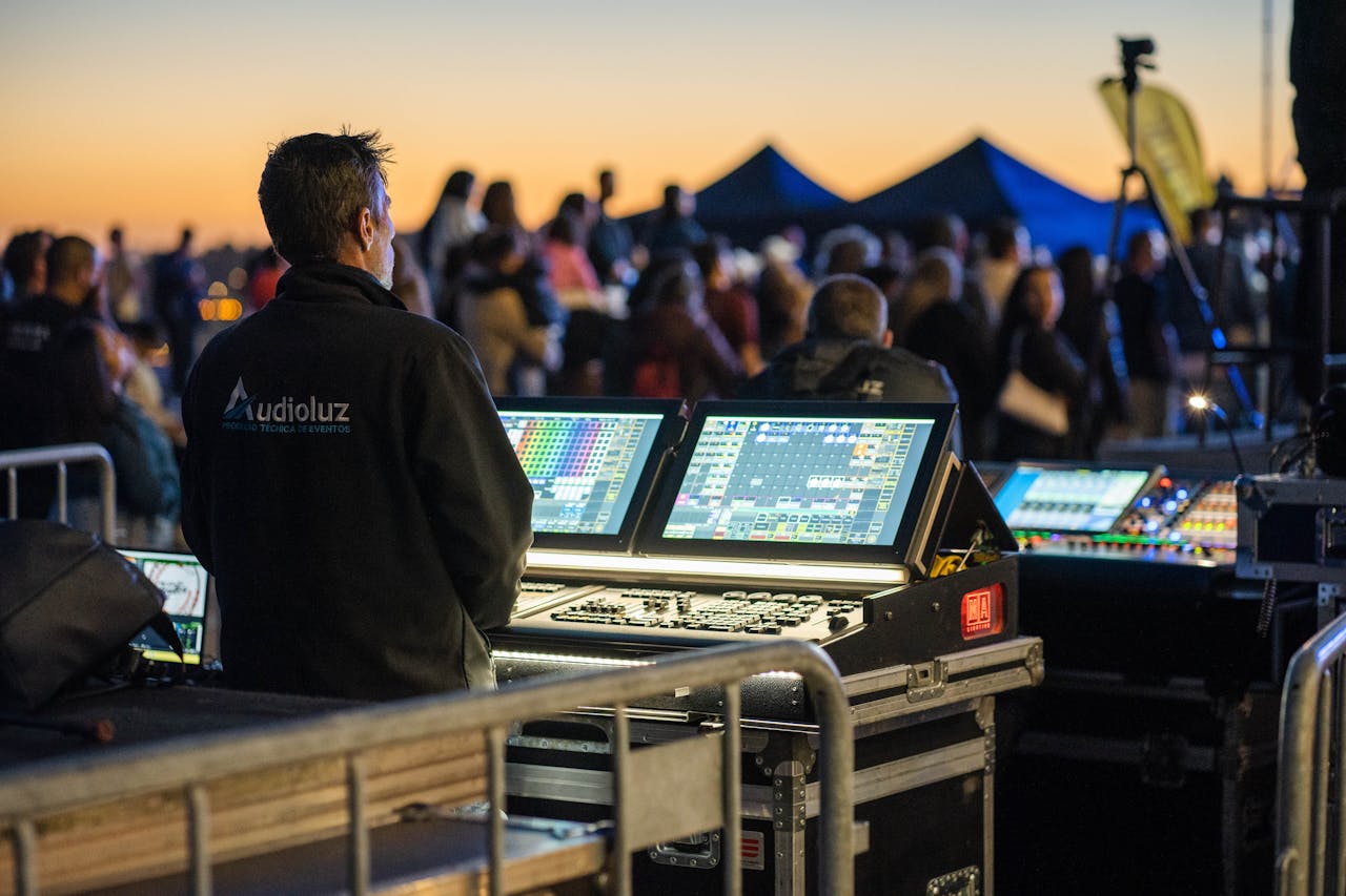 Technician managing sound and lighting panels during an outdoor event at sunset.