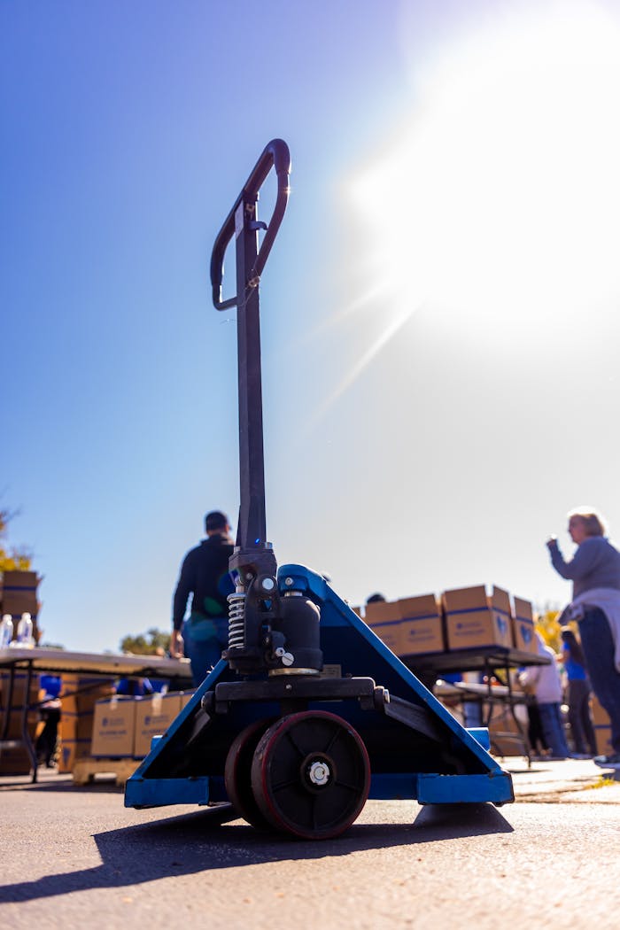 Offerings Pallet jack in focus during outdoor distribution event under bright sunlight.