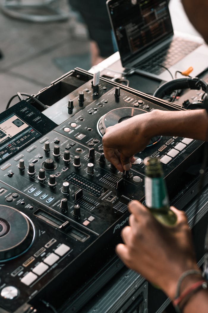 About Close-up of a DJ mixing music on a console while holding a beer bottle, creating a lively atmosphere.